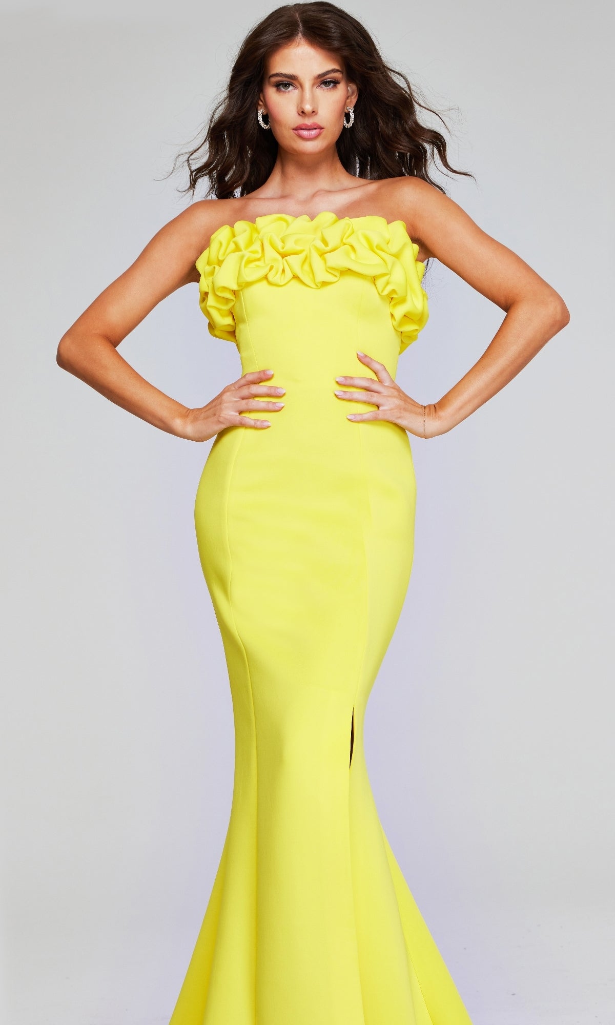 A woman poses with hands on hips in the Jovani 38922 Long Formal Dress, a strapless yellow gown with a form-fitting silhouette and ruffle detailing at the top, set against a plain background.